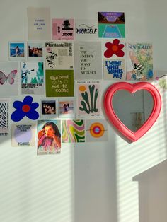 a heart shaped mirror hanging from the side of a wall with many pictures on it