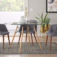 a glass dining table with wooden legs and grey chairs in front of a painting on the wall