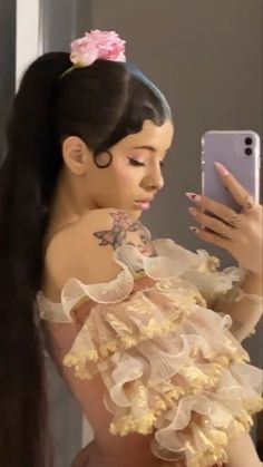 a woman taking a selfie with her cell phone while wearing a dress and flower in her hair