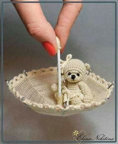 a hand holding a small teddy bear in a decorative bowl with thread on the edge