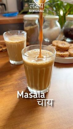 a person pouring milk into a glass on top of a wooden table next to cookies