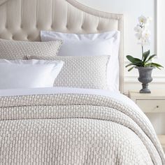 a bed with white sheets and pillows in a bedroom next to a vase with flowers