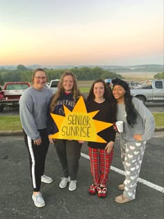 four girls standing in a parking lot holding a sign that says senior sunrise