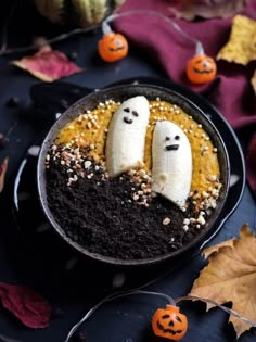 two bananas with faces carved into them sitting in a bowl surrounded by pumpkins and leaves