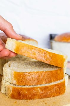 someone is holding a piece of white bread on a cutting board with the rest of it cut in half