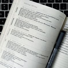 an open book sitting on top of a laptop computer next to a pen and keyboard