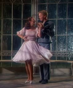 the man and woman are dancing together in front of some glass windows with rain falling on them