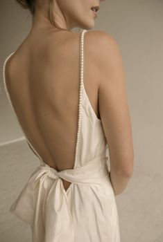 the back of a woman wearing a white dress with pearls on it's neck