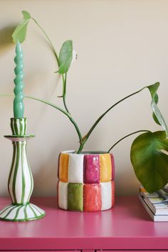 a pink table with two vases and a green plant