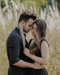 a man and woman hugging in the middle of a field with tall grass behind them