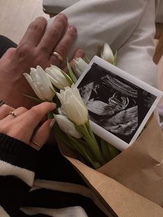 a woman is holding flowers in her hand and looking at an old photo on the table