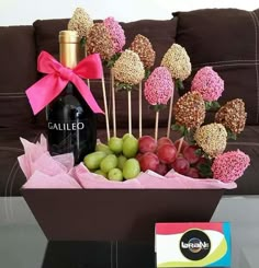 an arrangement of fruit and sweets in a basket on a table with a bottle of wine