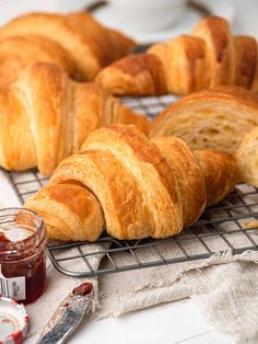 several croissants on a cooling rack with jam next to them and a knife