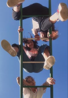 two people standing on top of a green ladder with their feet up in the air