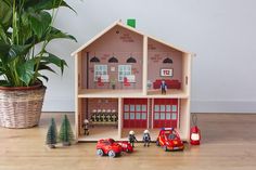 a toy house with cars and people in front of it next to a potted plant