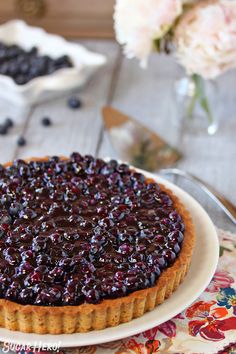 a blueberry cheesecake on a white plate with flowers in the backgroun