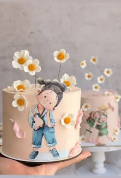 a person holding a cake with flowers on it and two other cakes in the background