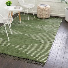 a green rug with white chairs and tables in front of a window next to a potted plant