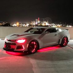 a white chevrolet camaro with red lights on it's side in front of a city skyline