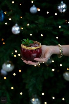 a person holding a drink in front of a christmas tree