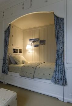 a white bed sitting under a window next to a wall mounted cabinet and night stand