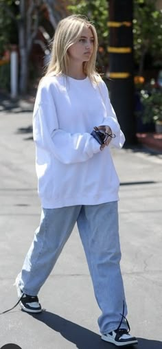 a woman in white sweater and jeans walking down the street with her hand on her hip