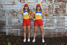 two young women dressed in costumes standing next to each other with their hands up and smiling