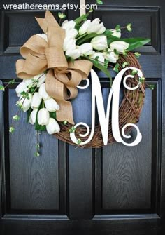 a wreath with the letter m on it and flowers hanging from it's front door