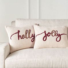 two pillows on a couch with the words holly jolly written in red thread across them