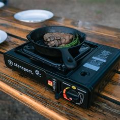 a small stove with some food cooking on it sitting on a wooden table next to plates