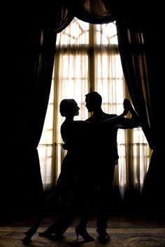 the silhouette of two people dancing in front of a large window with curtains and drapes