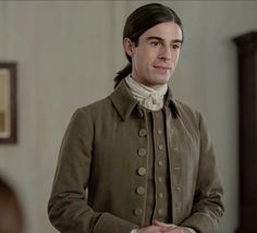 a man with long hair wearing a brown coat and white shirt standing in front of a mirror