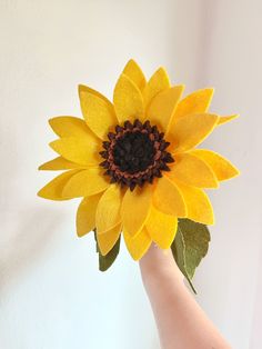 a hand holding a fake sunflower with leaves on it's tip and the center