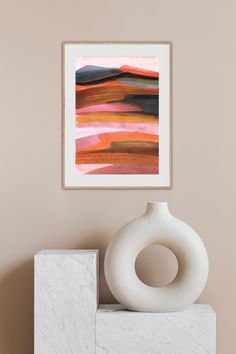 a white vase sitting on top of a marble block next to a framed art piece