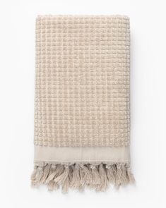 a beige and white blanket with fringes on the bottom, against a white background