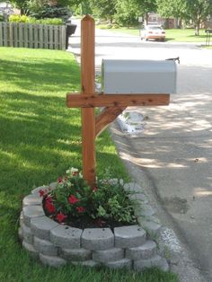 a mailbox sitting in the middle of a flower bed next to a cross on a sidewalk