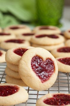 heart shaped cookies on a cooling rack with jam in the middle and green leaves behind them