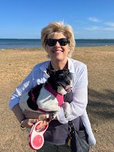 a woman holding a small dog in her arms on the beach near the ocean,