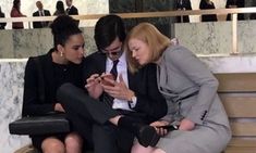 three women sitting on a bench looking at their cell phones while one looks at her phone