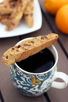 there is a cup of coffee and some cookies on the table next to oranges