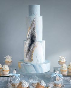 a white and blue cake sitting on top of a table next to cupcakes