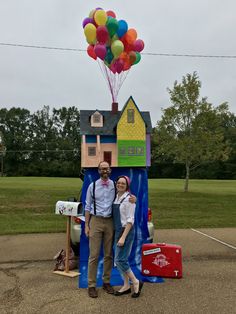 a man and woman standing in front of a fake house with balloons attached to it