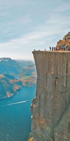 people are standing on the edge of a cliff overlooking a body of water and mountains