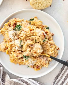 a white plate topped with pasta covered in cheese and sauce next to two slices of bread