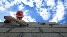 a man wearing a red hard hat and gloves on top of a brick wall next to a blue sky