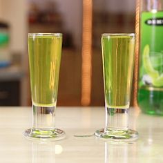 two glasses filled with green liquid sitting on top of a counter