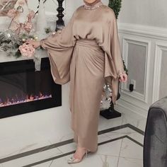 a woman standing in front of a fireplace wearing a tan dress and matching high heels