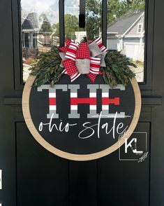 a black door with a red and white wreath hanging on it's side that says, this state