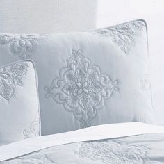 the comforter is made up with white embroidered sheets and pillow cases, along with two decorative pillows