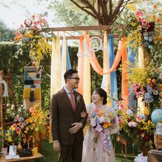 a man and woman standing next to each other in front of an arch with flowers